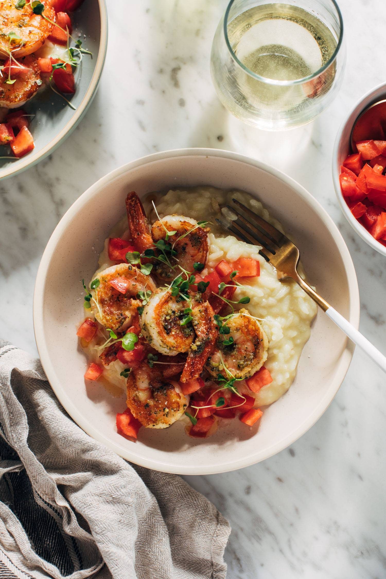 Pesto shrimp in a bowl with risotto and a fork and a glass of white wine on the side