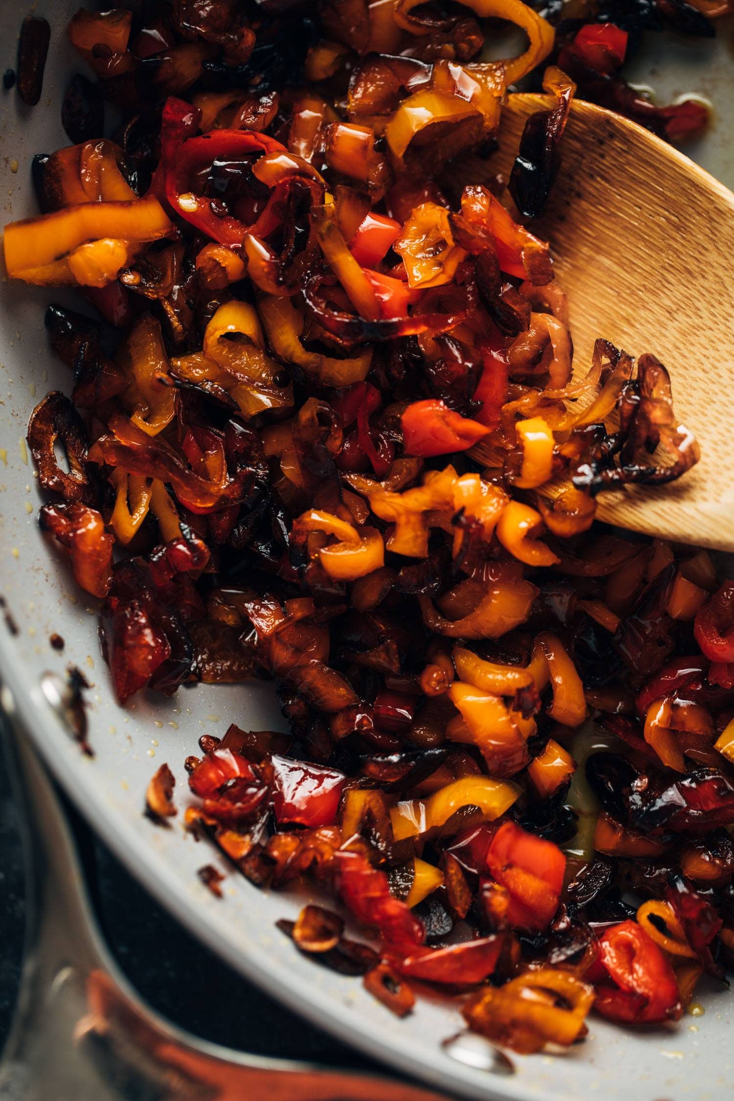 Peppers confit in a pan with a wooden spoon